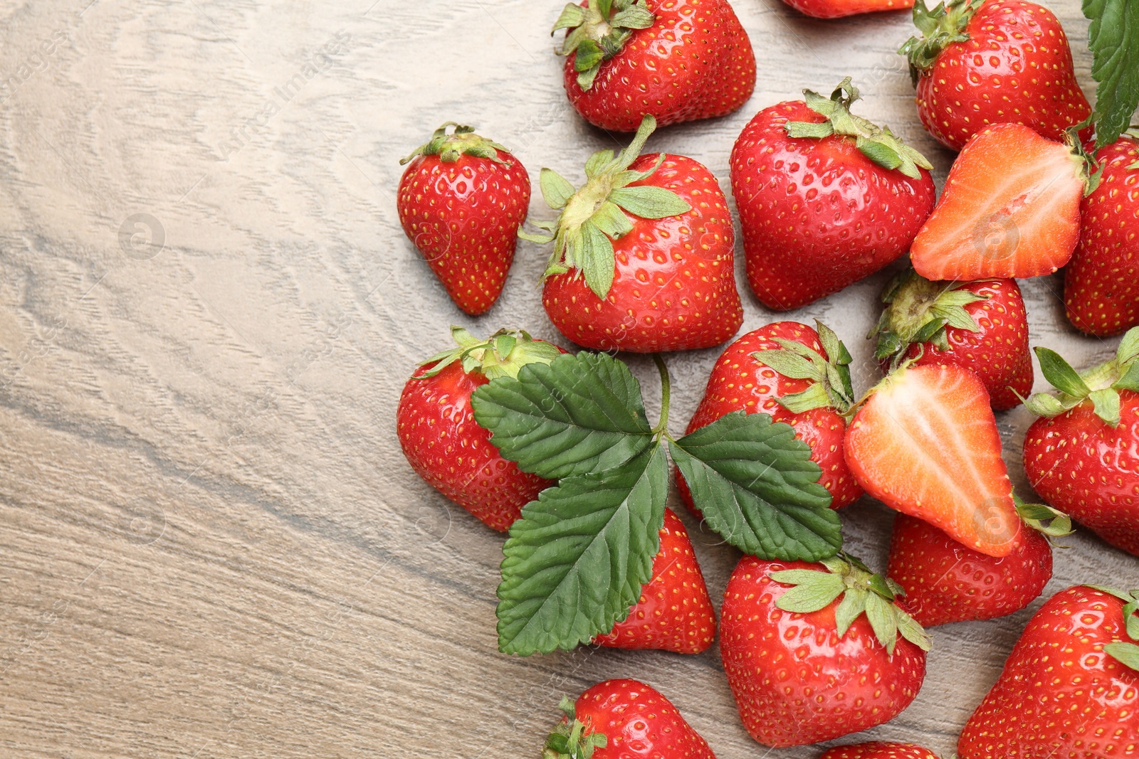 Delicious ripe strawberries and green leaves on wooden table, flat lay. Space for text Photo of Delicious ripe strawberries and green leaves on wooden table, flat lay. Space for text