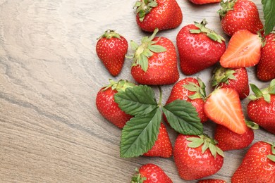 Photo of Delicious ripe strawberries and green leaves on wooden table, flat lay. Space for text