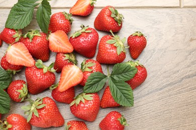 Photo of Delicious ripe strawberries and green leaves on wooden table, flat lay. Space for text