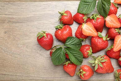 Photo of Delicious ripe strawberries and green leaves on wooden table, flat lay. Space for text