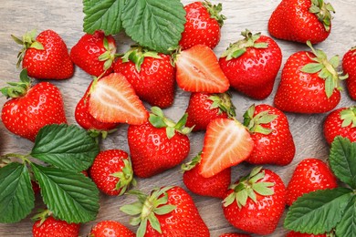 Photo of Delicious ripe strawberries and green leaves on wooden table, flat lay
