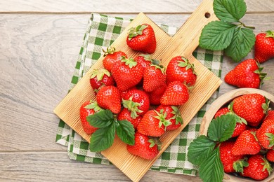 Photo of Delicious ripe strawberries and green leaves on wooden table, flat lay