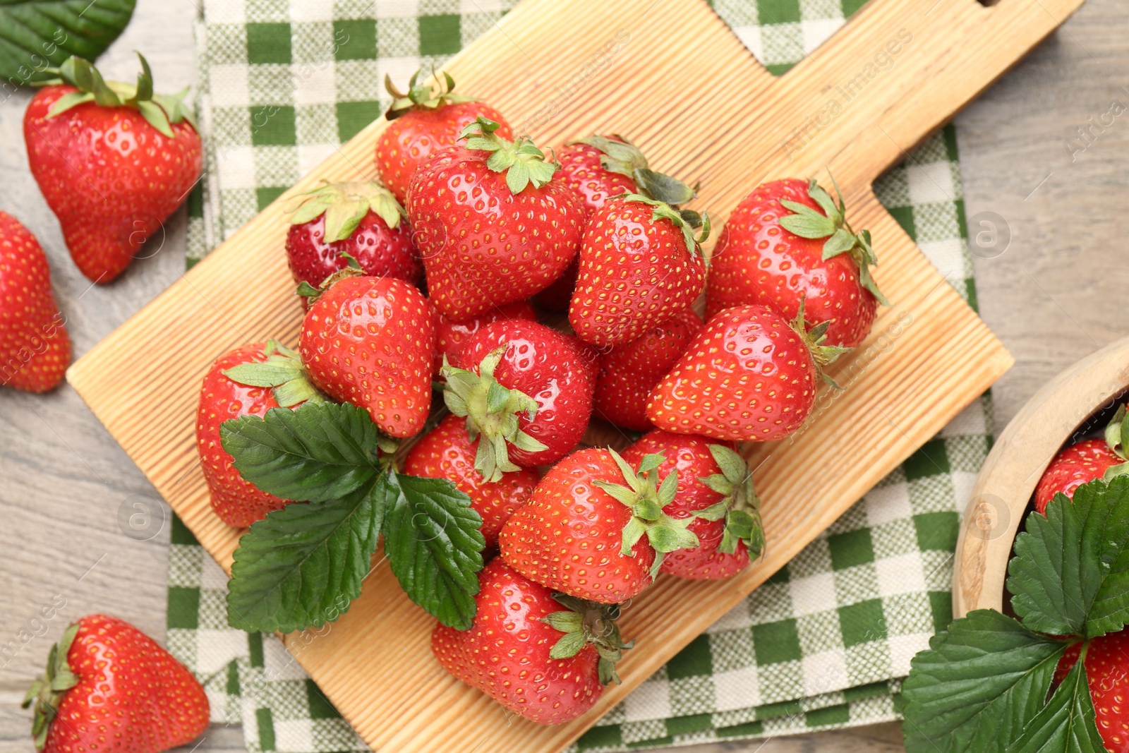 Delicious ripe strawberries and green leaves on wooden table, flat lay Photo of Delicious ripe strawberries and green leaves on wooden table, flat lay