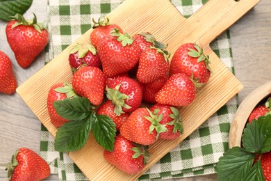 Photo of Delicious ripe strawberries and green leaves on wooden table, flat lay
