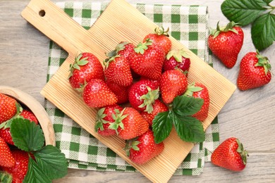 Photo of Delicious ripe strawberries and green leaves on wooden table, flat lay
