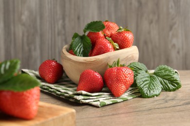Photo of Delicious ripe strawberries and green leaves on wooden table, closeup