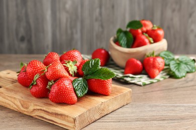 Photo of Delicious ripe strawberries and green leaves on wooden table, closeup. Space for text