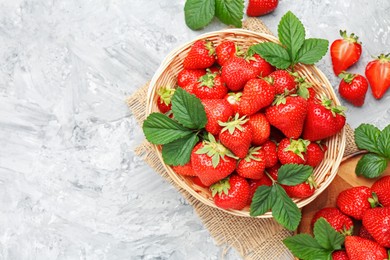 Photo of Delicious ripe strawberries and green leaves on grey table, flat lay. Space for text