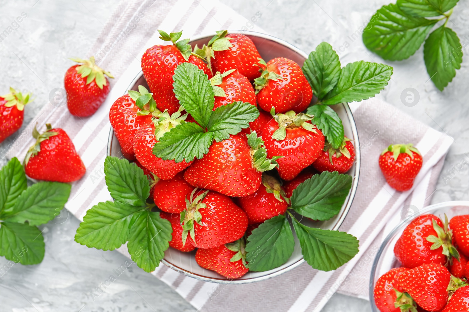 Delicious ripe strawberries and green leaves on grey table, flat lay Photo of Delicious ripe strawberries and green leaves on grey table, flat lay