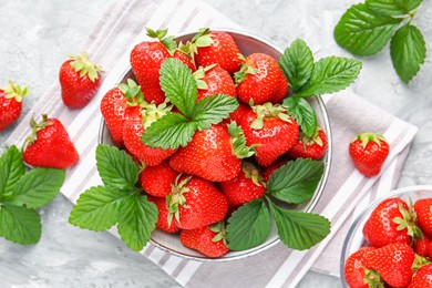 Photo of Delicious ripe strawberries and green leaves on grey table, flat lay