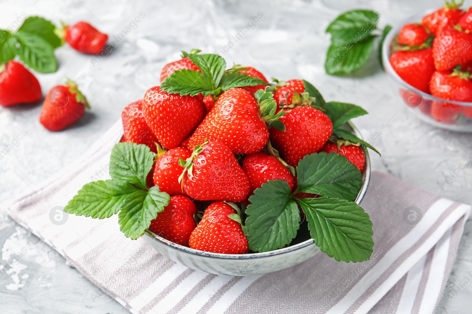 Delicious ripe strawberries and green leaves on grey table, closeup Photo of Delicious ripe strawberries and green leaves on grey table, closeup