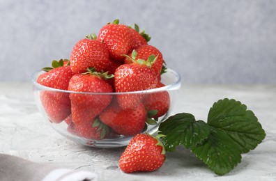 Photo of Delicious ripe strawberries and green leaves on grey table, closeup