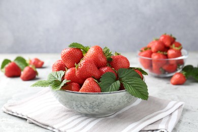 Photo of Delicious ripe strawberries and green leaves on grey table, closeup