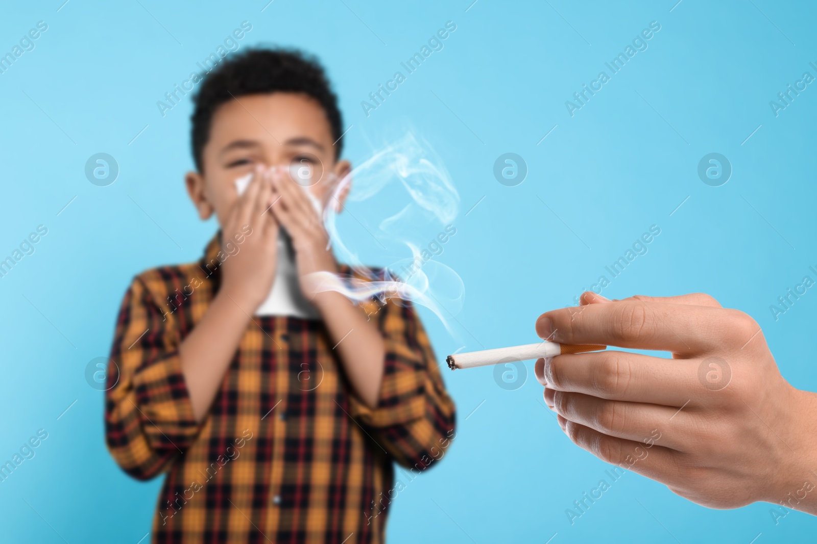 Passive smoking. Little boy covering his nose with tissue because of man smoking nearby on light blue background. Selective focus Image of Passive smoking. Little boy covering his nose with tissue because of man smoking nearby on light blue background. Selective focus