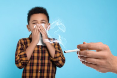 Image of Passive smoking. Little boy covering his nose with tissue because of man smoking nearby on light blue background. Selective focus