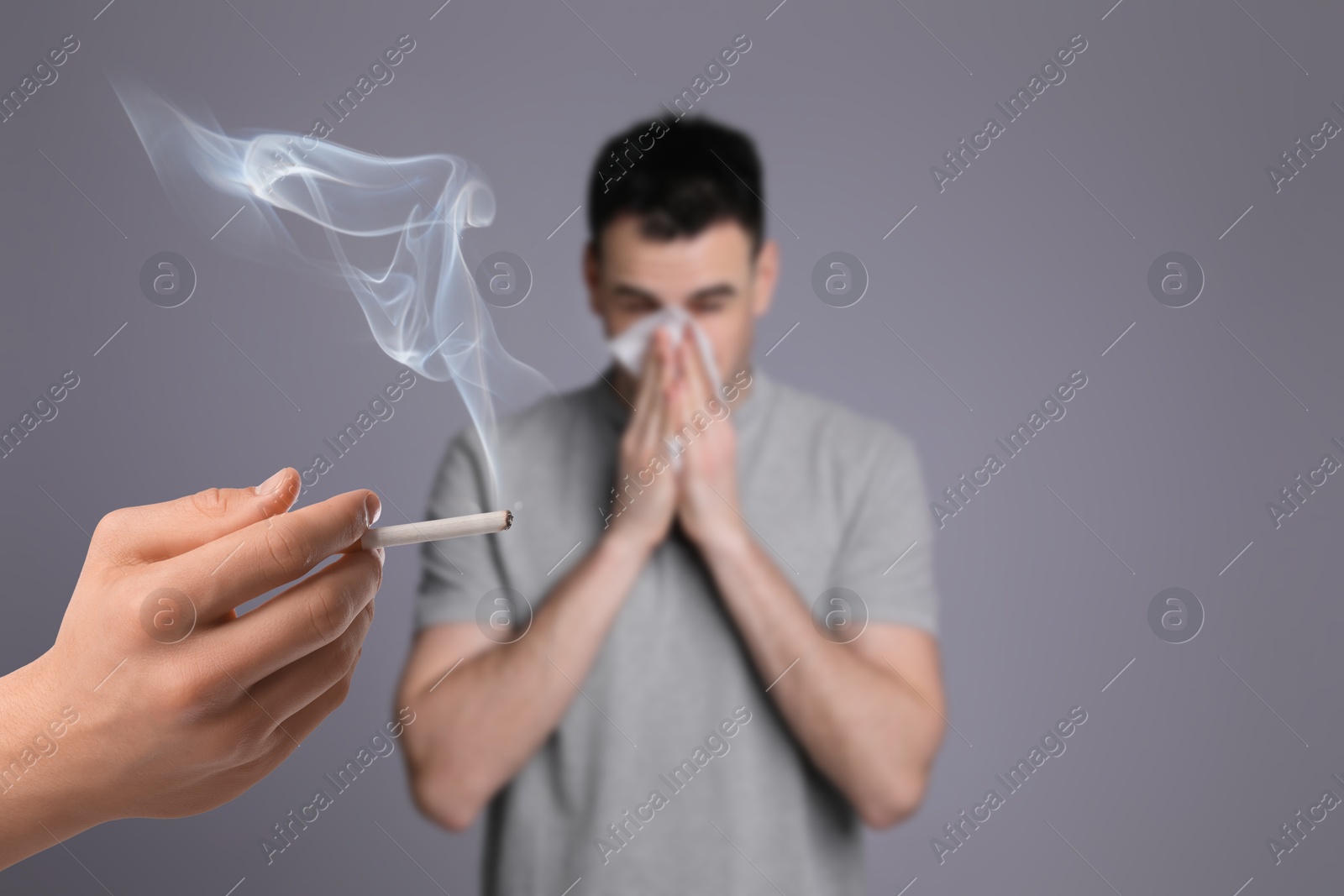 Passive smoking. Man covering his nose with tissue because of guy smoking nearby on grey background. Selective focus Image of Passive smoking. Man covering his nose with tissue because of guy smoking nearby on grey background. Selective focus