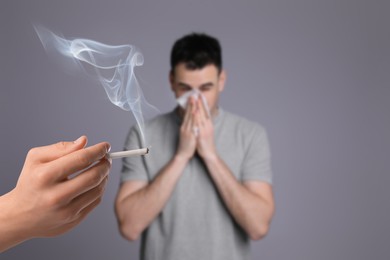 Image of Passive smoking. Man covering his nose with tissue because of guy smoking nearby on grey background. Selective focus