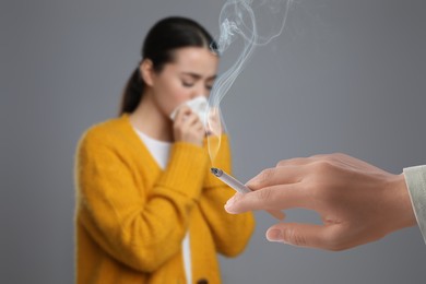 Image of Passive smoking. Girl covering her nose with tissue because of woman smoking nearby on grey background. Selective focus