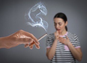 Image of Passive smoking. Woman coughing because of man smoking nearby on grey background. Selective focus