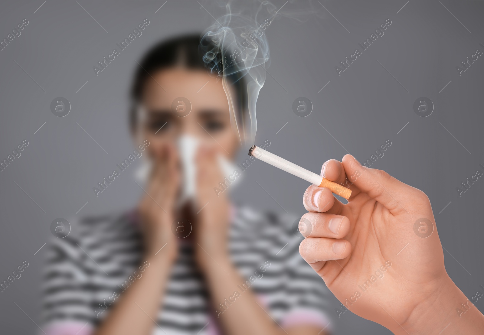 Passive smoking. Woman covering her nose with tissue because of man smoking nearby on grey background. Selective focus Image of Passive smoking. Woman covering her nose with tissue because of man smoking nearby on grey background. Selective focus