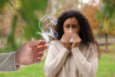 Image of Passive smoking. Girl covering her nose with tissue because of woman smoking nearby outdoors. Selective focus