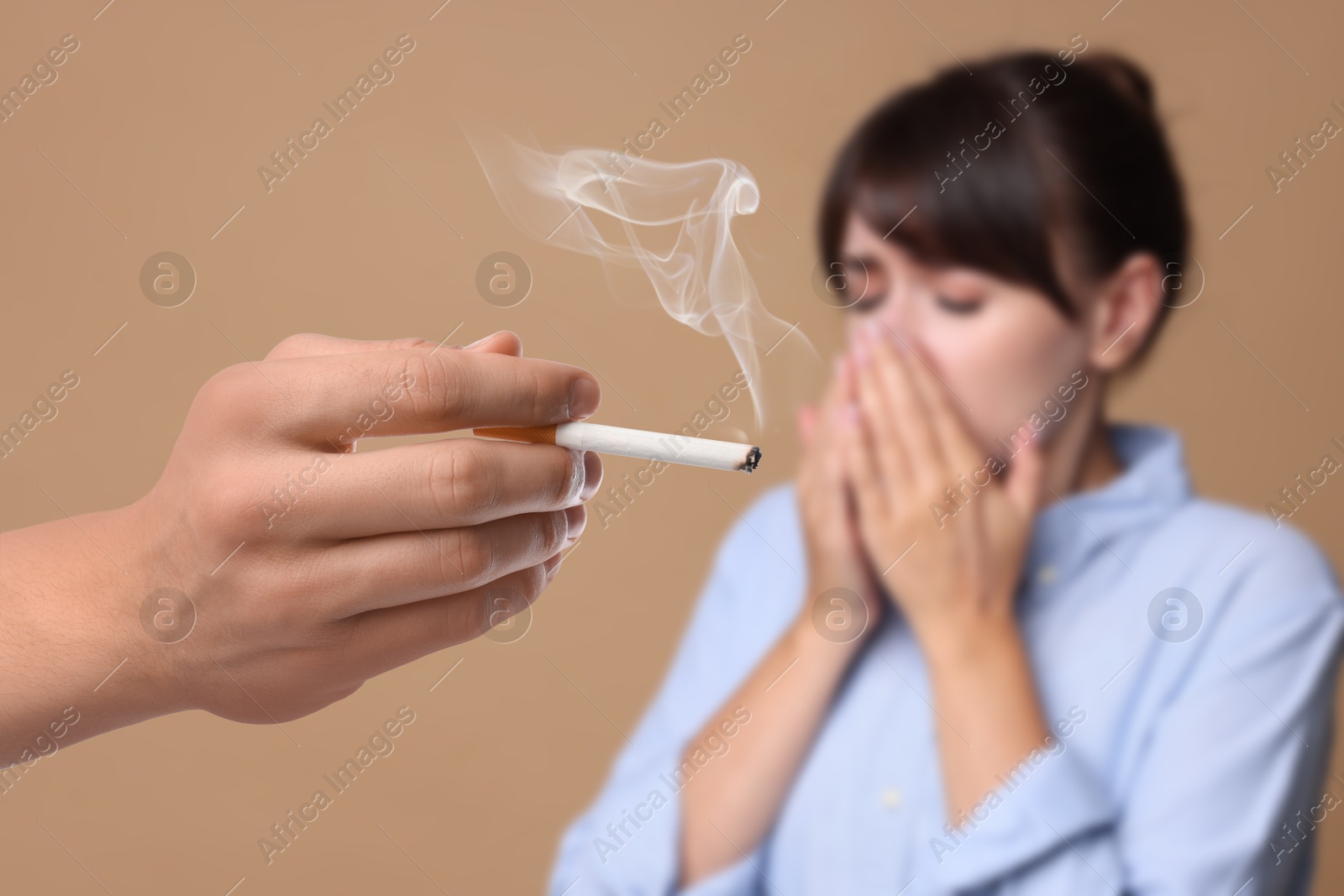Passive smoking. Woman covering her nose with hands because of man smoking nearby on pale brown background. Selective focus Image of Passive smoking. Woman covering her nose with hands because of man smoking nearby on pale brown background. Selective focus