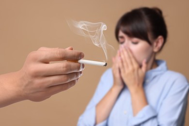 Image of Passive smoking. Woman covering her nose with hands because of man smoking nearby on pale brown background. Selective focus