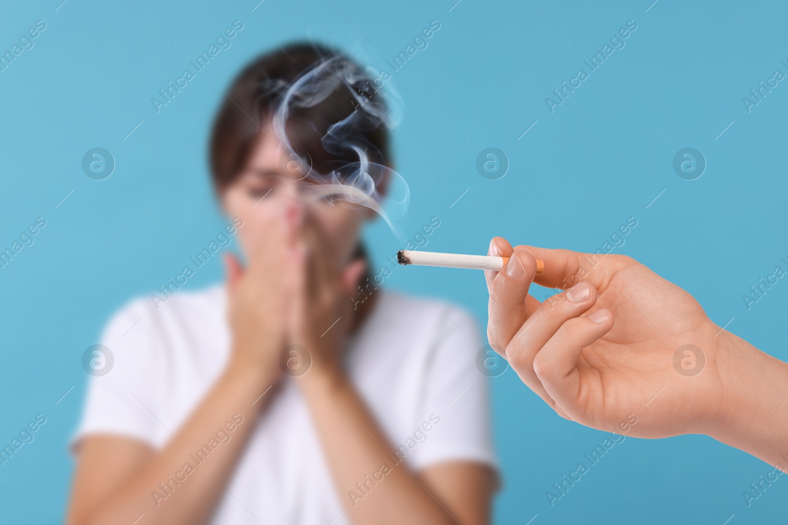 Passive smoking. Woman covering her nose with hands because of man smoking nearby on light blue background. Selective focus Image of Passive smoking. Woman covering her nose with hands because of man smoking nearby on light blue background. Selective focus
