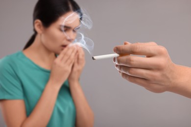 Image of Passive smoking. Woman coughing because of man smoking nearby on grey background. Selective focus