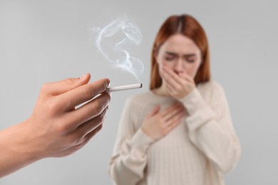 Image of Passive smoking. Woman coughing because of man smoking nearby on light grey background. Selective focus