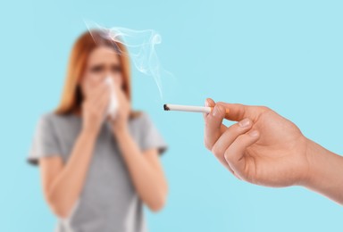 Image of Passive smoking. Woman covering her nose with tissue because of man smoking nearby on light blue background. Selective focus