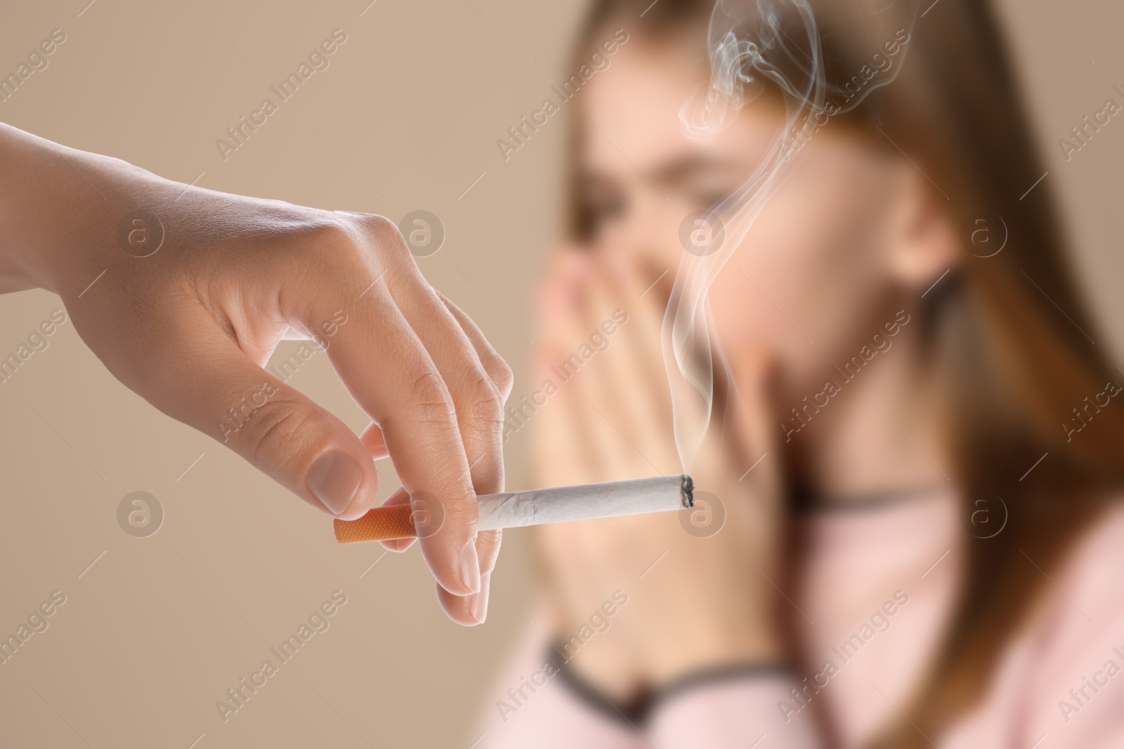 Passive smoking. Girl coughing because of woman smoking nearby on beige background. Selective focus Image of Passive smoking. Girl coughing because of woman smoking nearby on beige background. Selective focus
