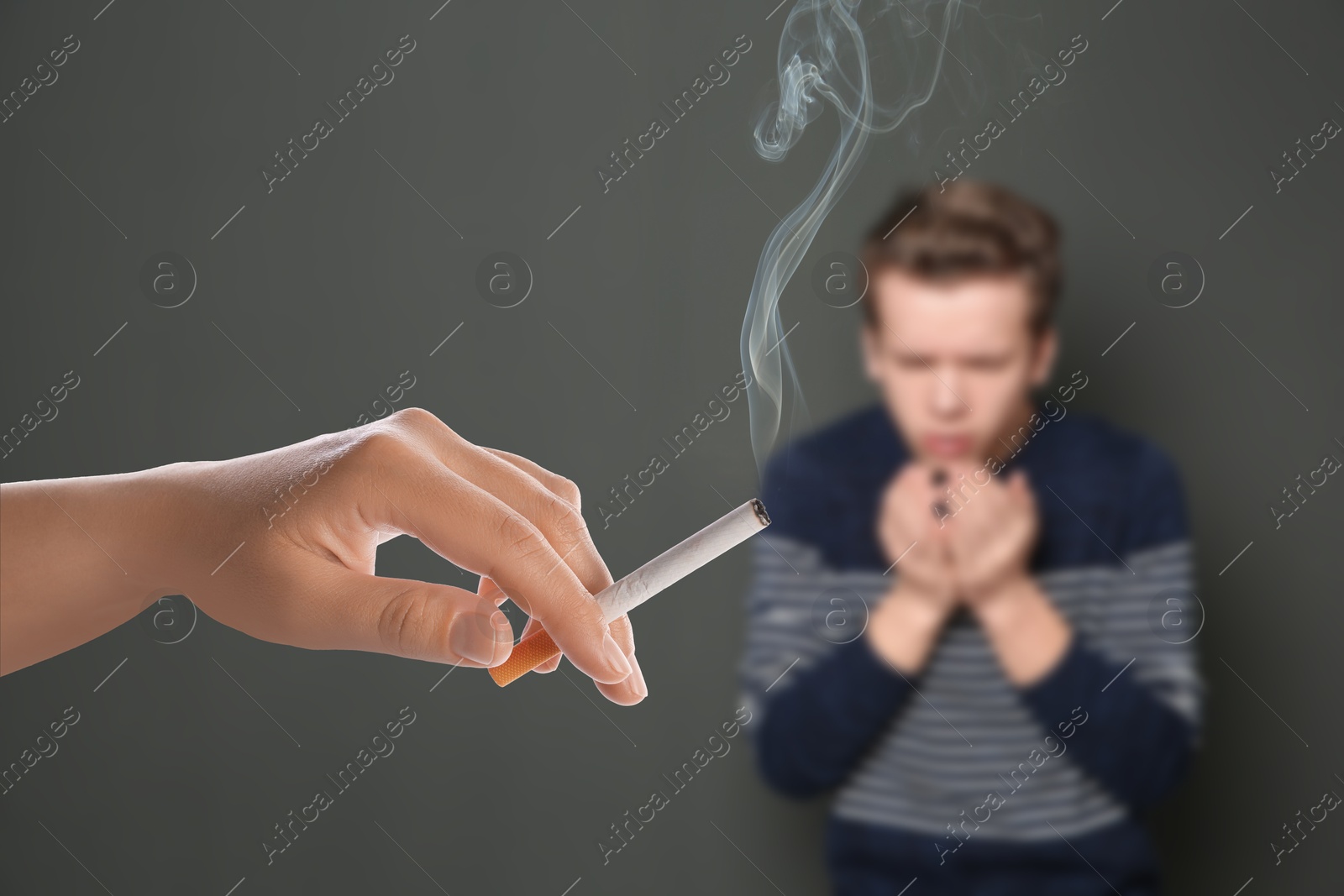 Passive smoking. Boy coughing because of woman smoking nearby on grey background. Selective focus Image of Passive smoking. Boy coughing because of woman smoking nearby on grey background. Selective focus