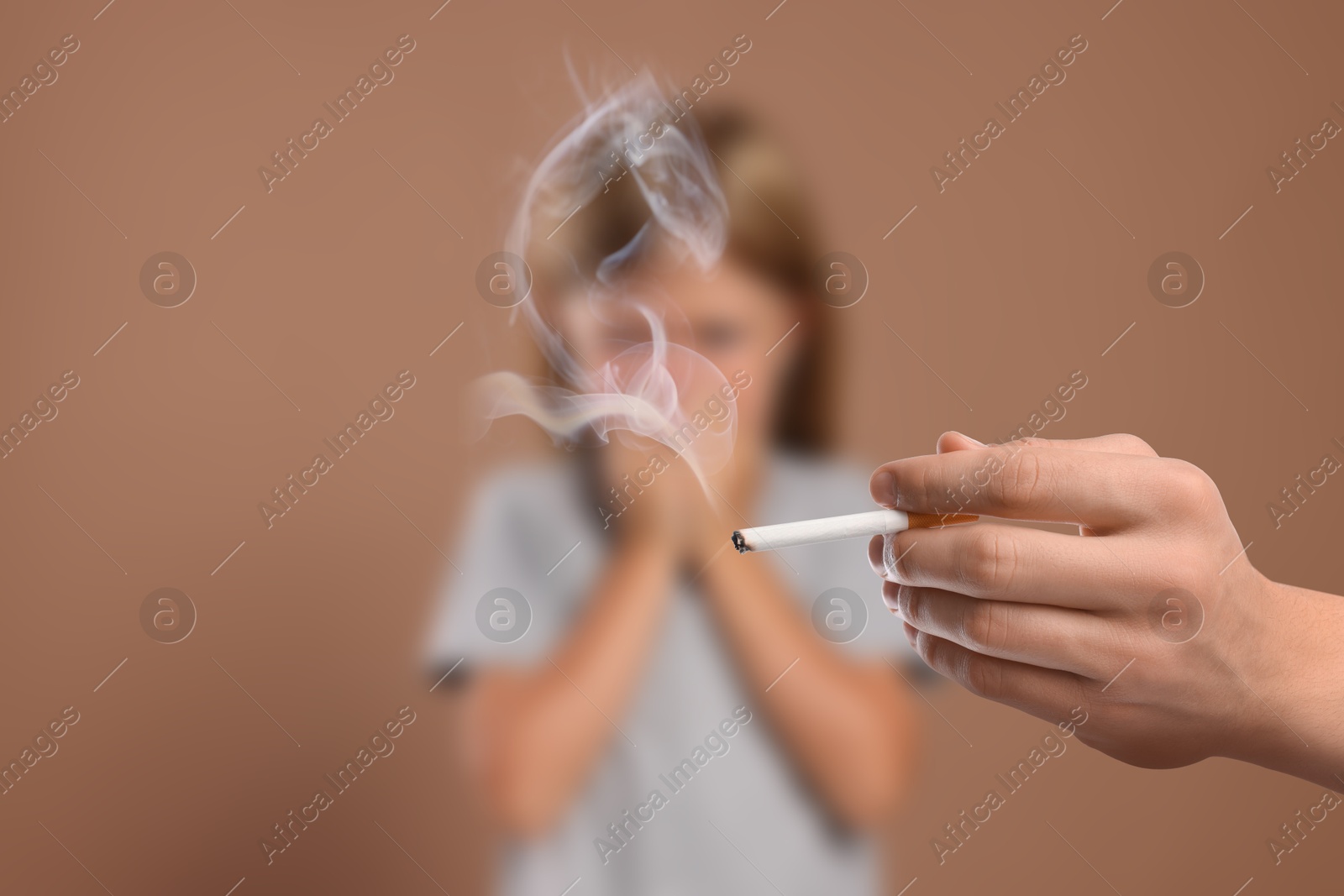 Passive smoking. Little girl covering her nose with hands because of man smoking nearby on pale brown background. Selective focus Image of Passive smoking. Little girl covering her nose with hands because of man smoking nearby on pale brown background. Selective focus