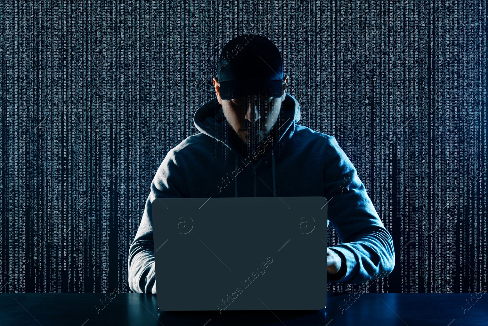 Cyber attack. Hacker working on laptop at table. Digital code behind him Image of Cyber attack. Hacker working on laptop at table. Digital code behind him