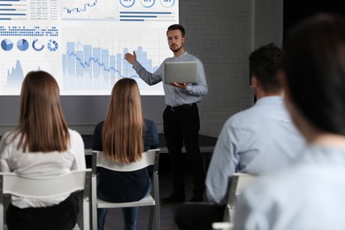 Image of Business trainer giving lecture using video projector in conference room. Graphs on projection screen