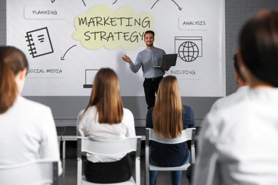Image of Business trainer giving lecture using video projector in conference room. Marketing strategy scheme with illustrations on projection screen