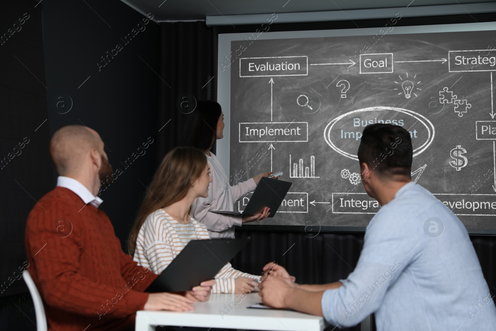 Business trainer giving lecture using video projector in conference room. Scheme with illustrations on projection screen Image of Business trainer giving lecture using video projector in conference room. Scheme with illustrations on projection screen
