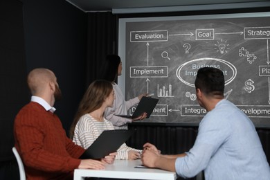 Image of Business trainer giving lecture using video projector in conference room. Scheme with illustrations on projection screen