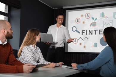 Image of Business trainer giving lecture using video projector in conference room. Fintech word and illustrations on projection screen