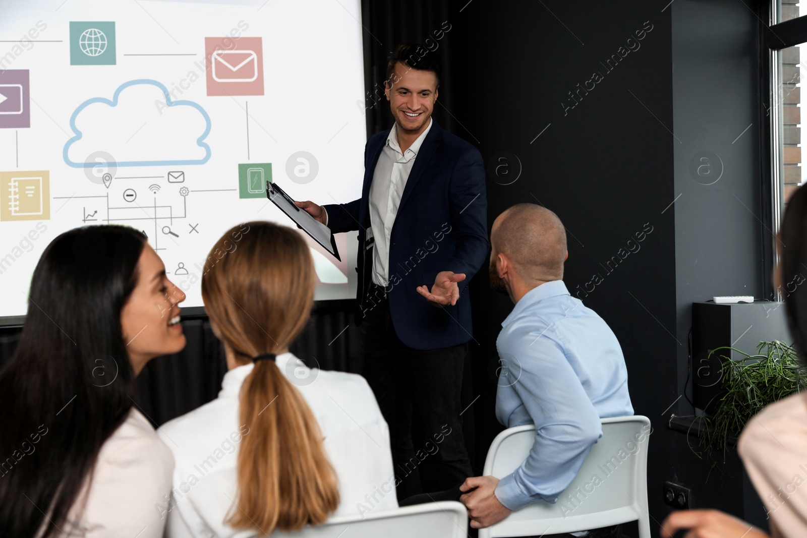 Business trainer giving lecture using video projector in conference room. Scheme with illustrations on projection screen Image of Business trainer giving lecture using video projector in conference room. Scheme with illustrations on projection screen