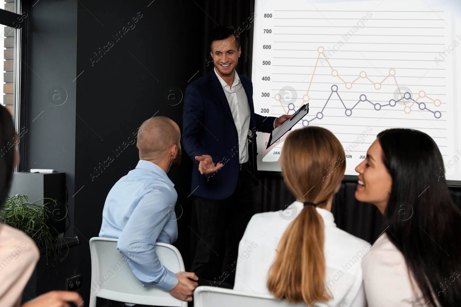 Business trainer giving lecture using video projector in conference room. Graph on projection screen Image of Business trainer giving lecture using video projector in conference room. Graph on projection screen