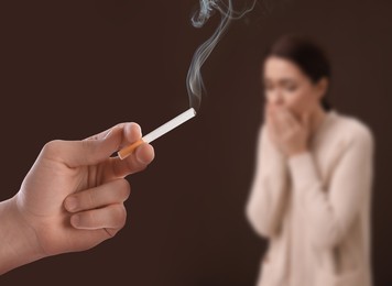 Image of Passive smoking. Woman coughing because of man smoking nearby on brown background. Selective focus