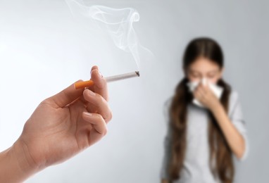 Image of Passive smoking. Little girl covering her nose with tissue because of woman smoking nearby on light background. Selective focus