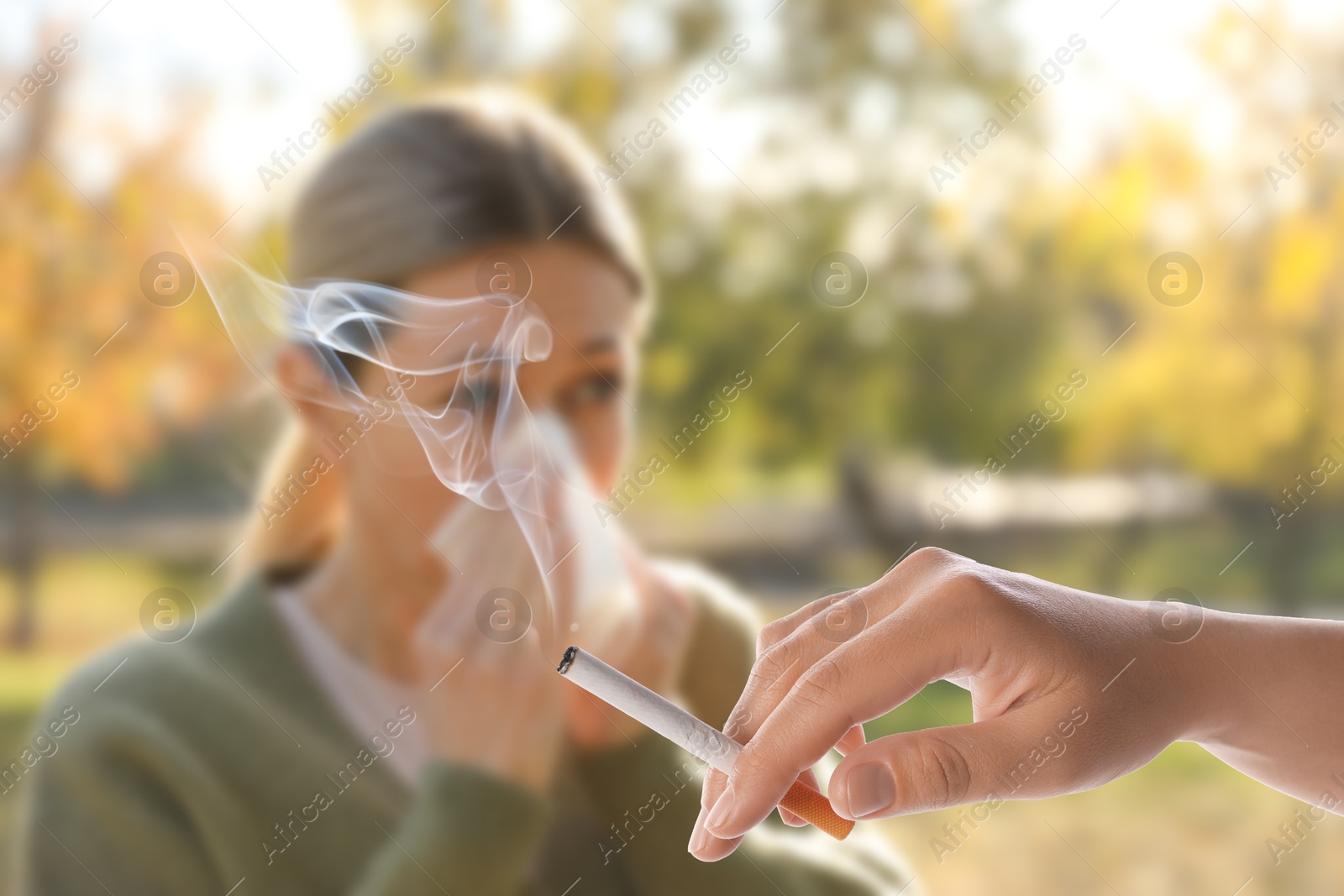 Passive smoking. Woman covering her nose with tissue because of girl smoking nearby outdoors. Selective focus Image of Passive smoking. Woman covering her nose with tissue because of girl smoking nearby outdoors. Selective focus
