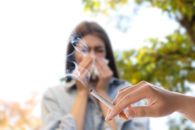 Image of Passive smoking. Girl covering her nose with tissue because of woman smoking nearby outdoors. Selective focus