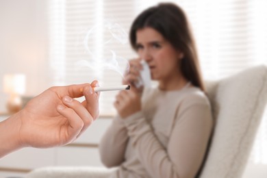 Image of Passive smoking. Woman covering her nose with tissue because of man smoking nearby at home. Selective focus