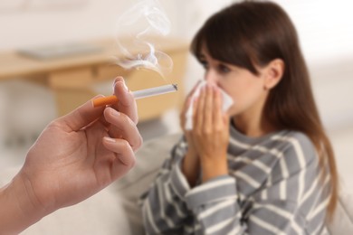 Image of Passive smoking. Girl covering her nose with tissue because of woman smoking nearby at home. Selective focus