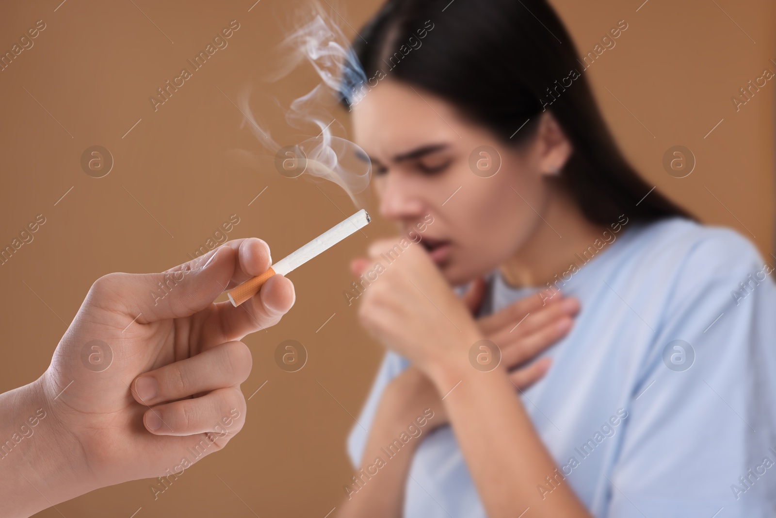 Passive smoking. Woman coughing because of man smoking nearby on pale brown background. Selective focus Image of Passive smoking. Woman coughing because of man smoking nearby on pale brown background. Selective focus