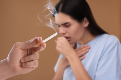 Image of Passive smoking. Woman coughing because of man smoking nearby on pale brown background. Selective focus